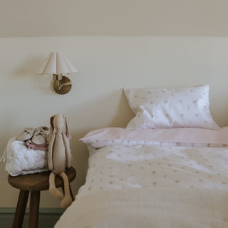Bedroom with a bed featuring pink bedding and a small stool with a plush toy and bag against a wall-mounted lamp.