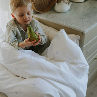 Child holding a green pear in a cozy indoor setting under a toddler duvet embroidered with blue stars. 