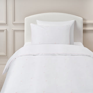 White bedding set pink embroidered hearts on a bed with a neutral-colored wall in the background.