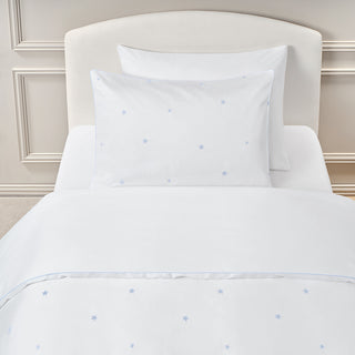 White bedding set with subtle blue embroidered star patterns on a bed with a beige headboard.