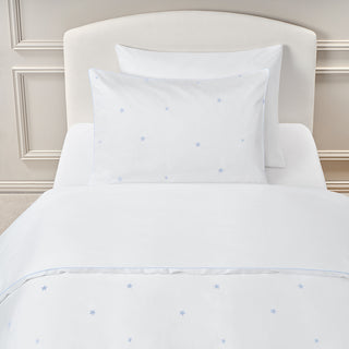 White bedding set with Embroidered Stars print on a bed with a beige headboard.
