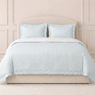 Picnic gingham in blue duvet set on a bed with matching pillows against a beige wall.