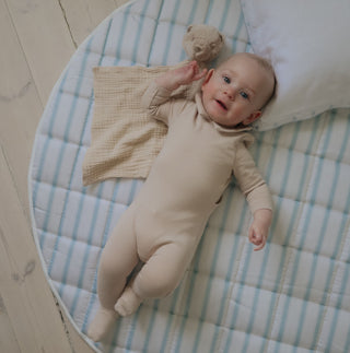 Baby lying on a striped play mat with a teddy bear and blanket