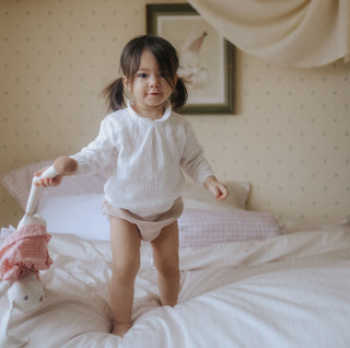 Child standing on pink and white bed holding a toy, 