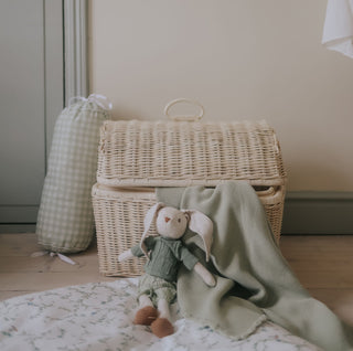 Wicker basket with a plush toy and green blanket on a wooden floor.