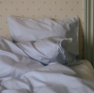Blue set of bedding on a bed against a wallpapered wall. 