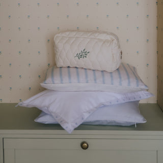 Stack of pillows and a pouch on a dresser with floral wallpaper.