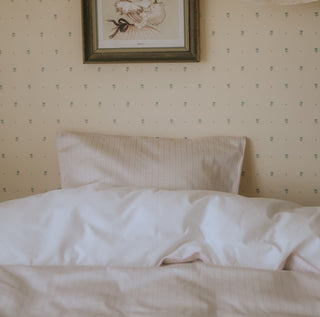 Neatly made bed with pink and white bedding against a wall with decorative wallpaper and a framed picture.