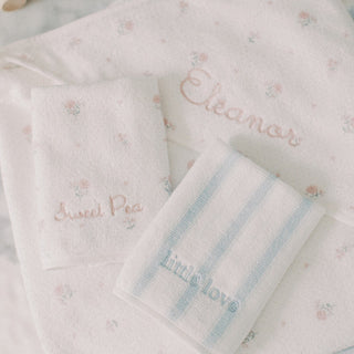 Three personalized baby washcloths in soft pastel colors, including a floral print, a light pink embroidered name, and light blue stripes with a blue embroidered name, arranged on a white background.