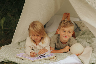 Two children inside a tent, one reading a book and the other smiling.