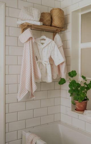 Bathroom with white tiled walls, a wooden shelf with towels and baskets, and a potted plant.