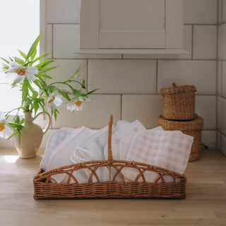 Wicker basket with baby blankets on a wooden floor, with a vase of flowers and woven baskets in the background.
