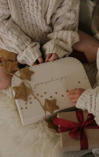 Two people in cozy sweaters holding a heart-shaped gift box with gold stars and 'gooselings' text.