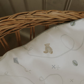 Close-up of a wicker basket with a decorative pillow featuring teddy bear illustrations.