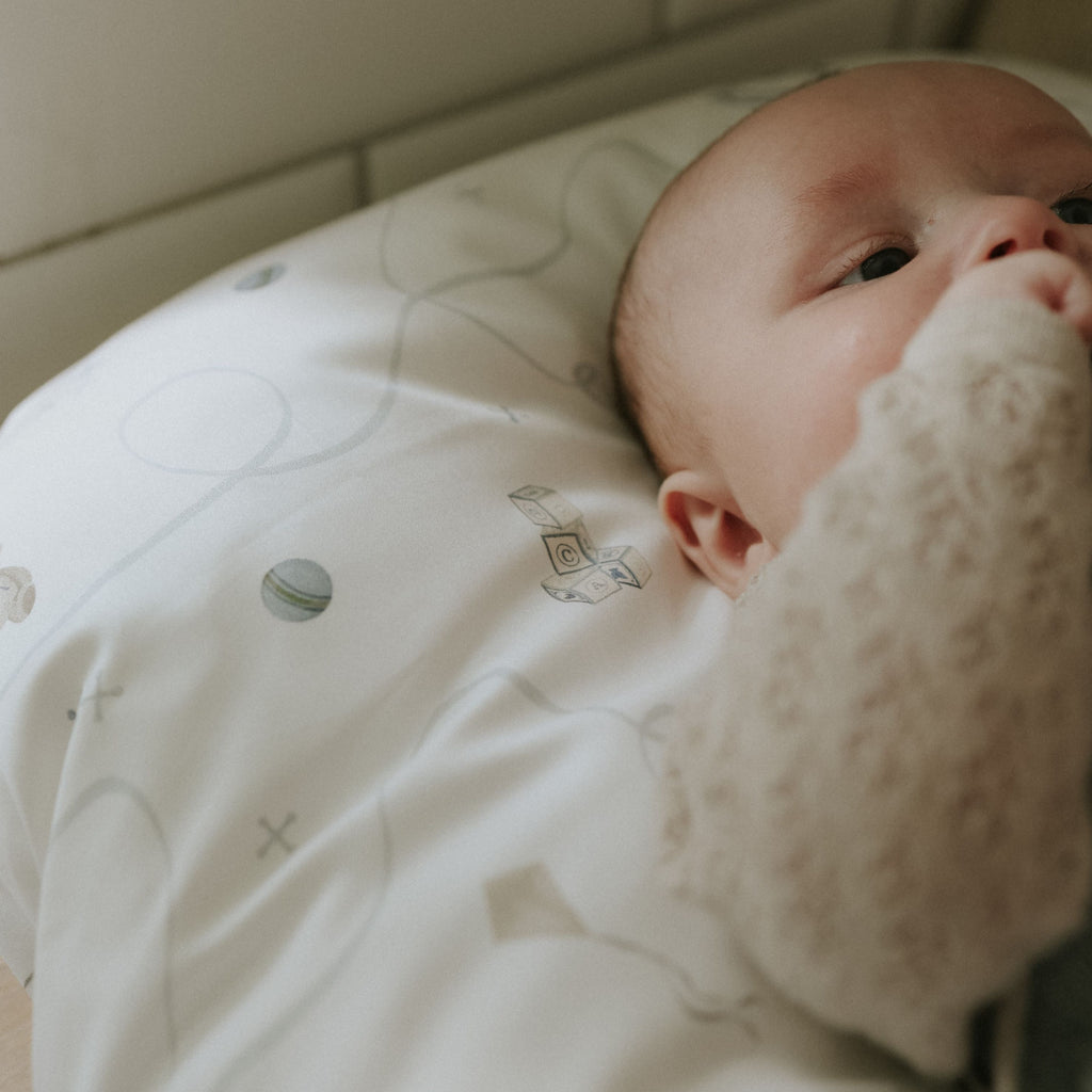 Baby lying on a white blanket with a soft toy