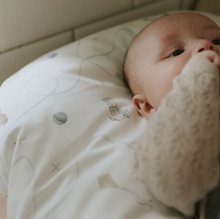 Baby lying on a white blanket with a soft toy