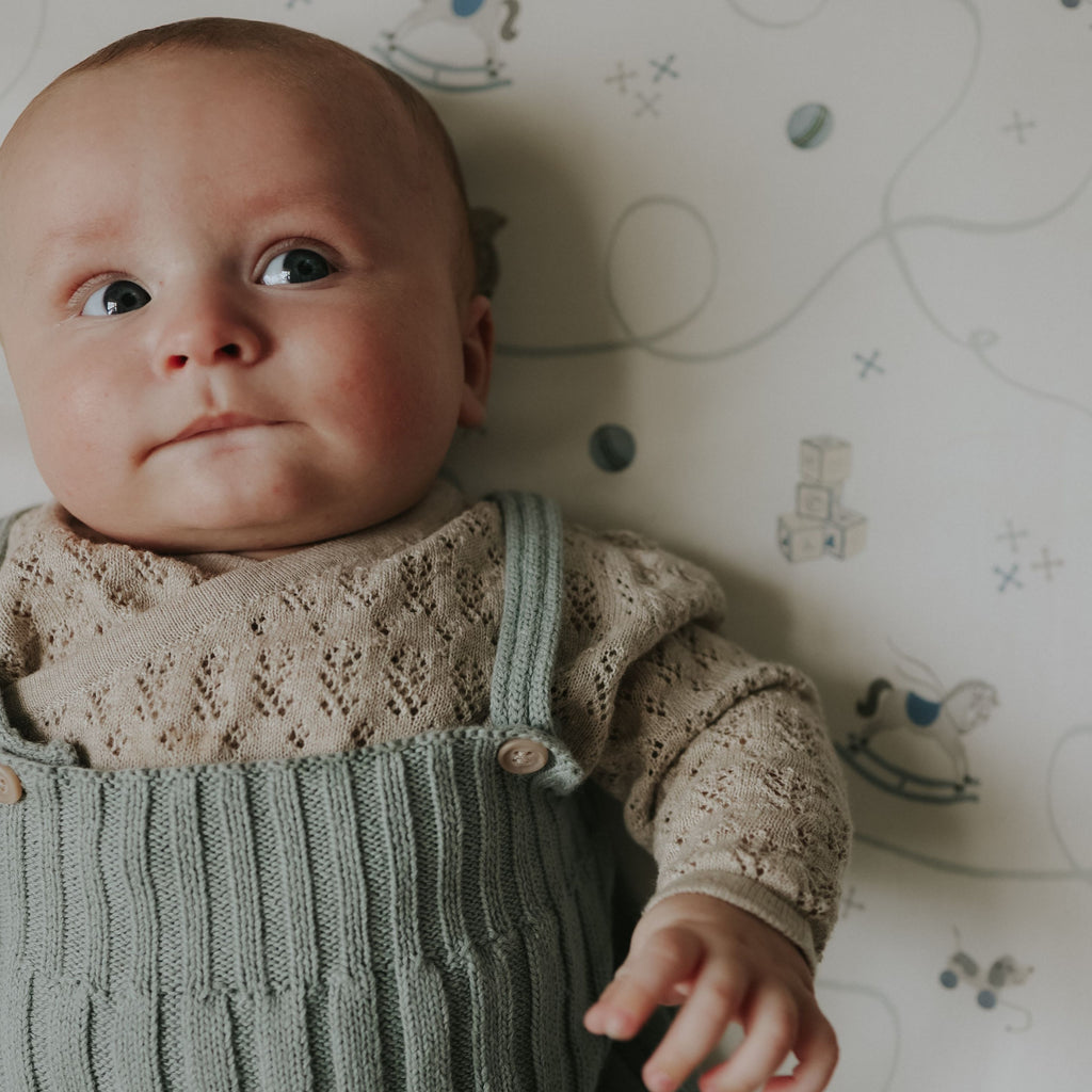 Baby wearing a knitted outfit with a patterned crib sheet background