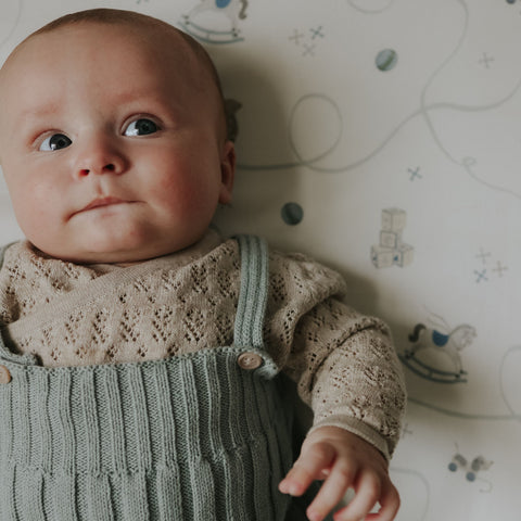 Baby wearing a knitted outfit with a patterned crib sheet background