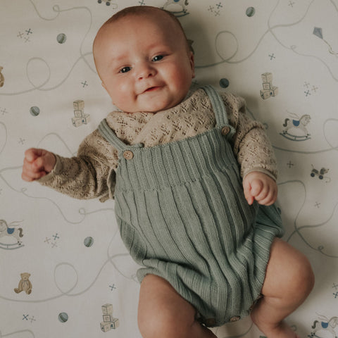 Baby wearing a green romper on a patterned crib sheet