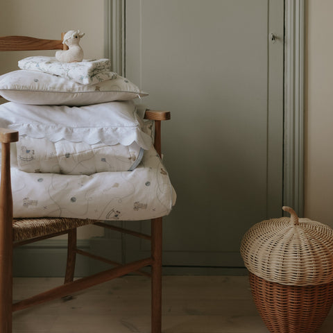 Stack of white baby blankets and pillows on a wooden chair against a plain wall.