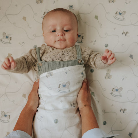 Baby in a knitted outfit lying on a crib with a patterned sheet