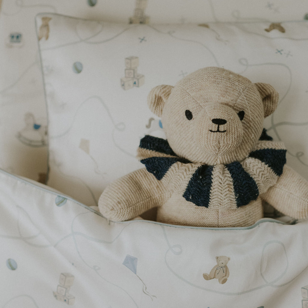 Knitted teddy bear with a striped scarf on a patterned blanket