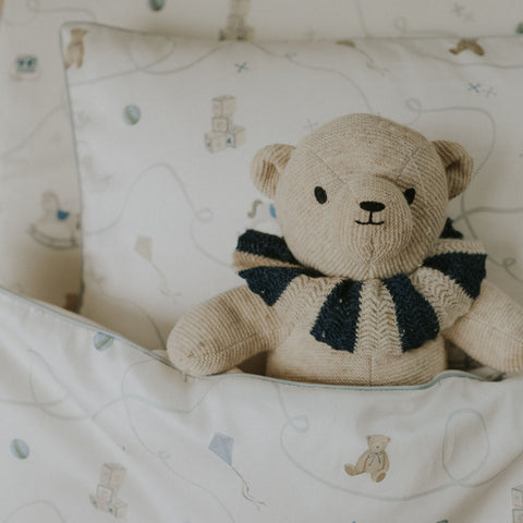 Knitted teddy bear with a striped scarf on a patterned blanket