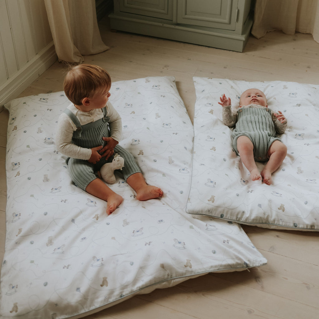 Two children in matching outfits sitting on patterned mats in a room.