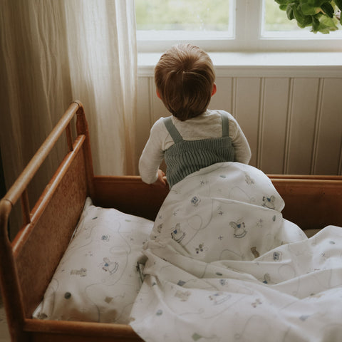 Child in a crib with patterned bedding and a window in the background