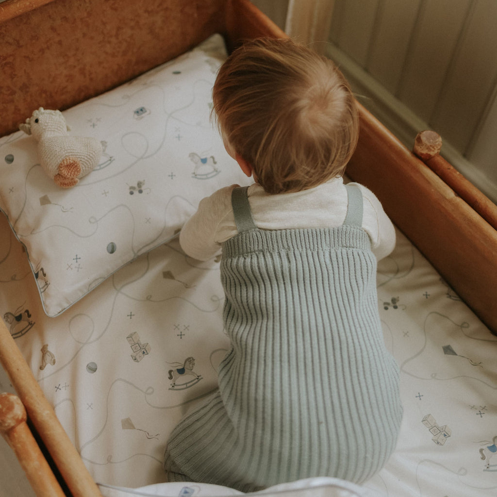 Child in a crib with a patterned sheet and pillow