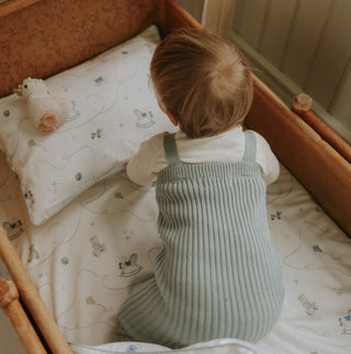 Child in a crib with a patterned sheet and pillow