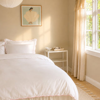Neatly made bed in a bedroom with a side table and window.