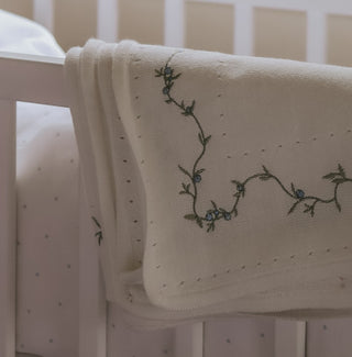 Embroidered blanket with floral design draped over a crib