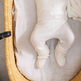 Close-up of a white ribbed knit pant on baby laying in woven bassinet.