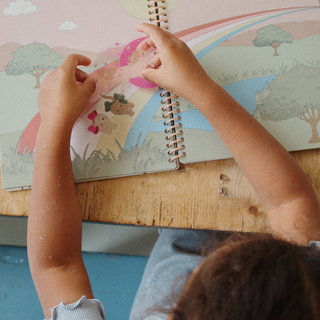 Child's hands interacting with a colorful children's book on a wooden table.