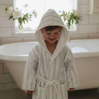 Child wearing a striped bathrobe in a bathroom with a bathtub and flowers.