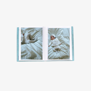 Open photo album showing two images of a baby on a textured blanket.