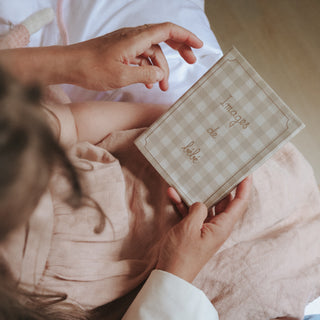 Person holding a checkered photo album  with 'Images de bebe' text, sitting on a pink blanket.