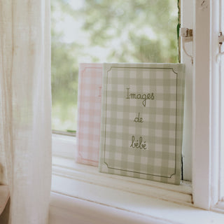 Checkered photo album titled 'Images de bebe' on a windowsill with a blurred green outdoor background.