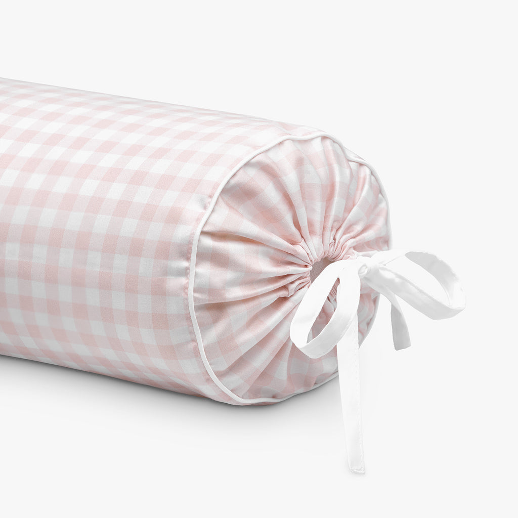 Pink checkered cylindrical pillow with a white ribbon on a light gray background