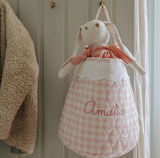 Pink checkered baby bag with a plush bunny toy hanging on a door