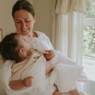 Woman holding a baby in a softly lit room with a window in the background