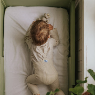 Child lying in a crib with a white mattress and green crib frame.