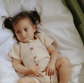 Child wearing a beige romper lying on a white bed