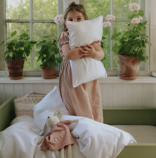 Child holding a pillow in a room with plants and a window