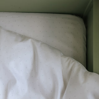 Close-up of a mattress with a white fitted sheet and green wall in the background