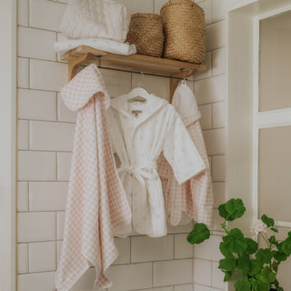 Bathrobes hanging on a rack against a tiled bathroom wall with a plant in the corner.