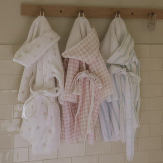 Three children's robes hanging on a rack against a tiled wall.