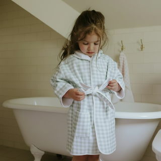 Child in a checkered robe standing by a bathtub in a bathroom.
