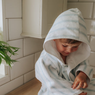 Child wearing a striped hooded bathrobe in a bathroom setting